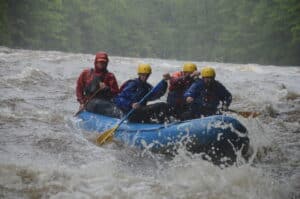 Rafting team paddling through whitewater in heavy rain on the Upper Yough, Greg in the front left position
