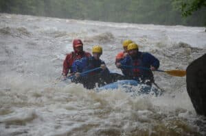 Rafting team paddling out of whitewater churn with the guide in red visible behind